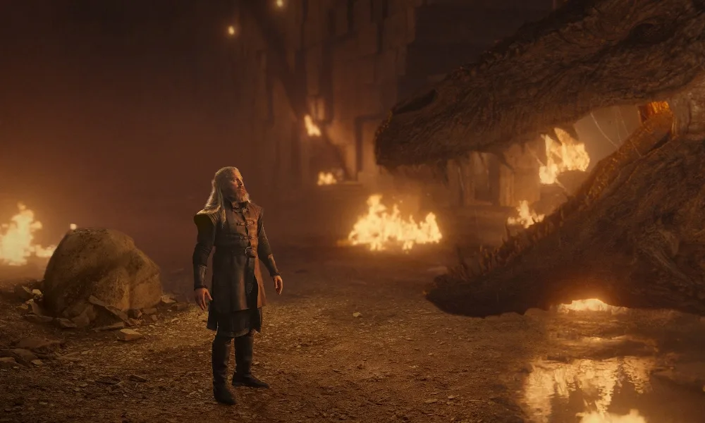Vermithor1000x600 A man standing in front of a dragon, surrounded by fire.