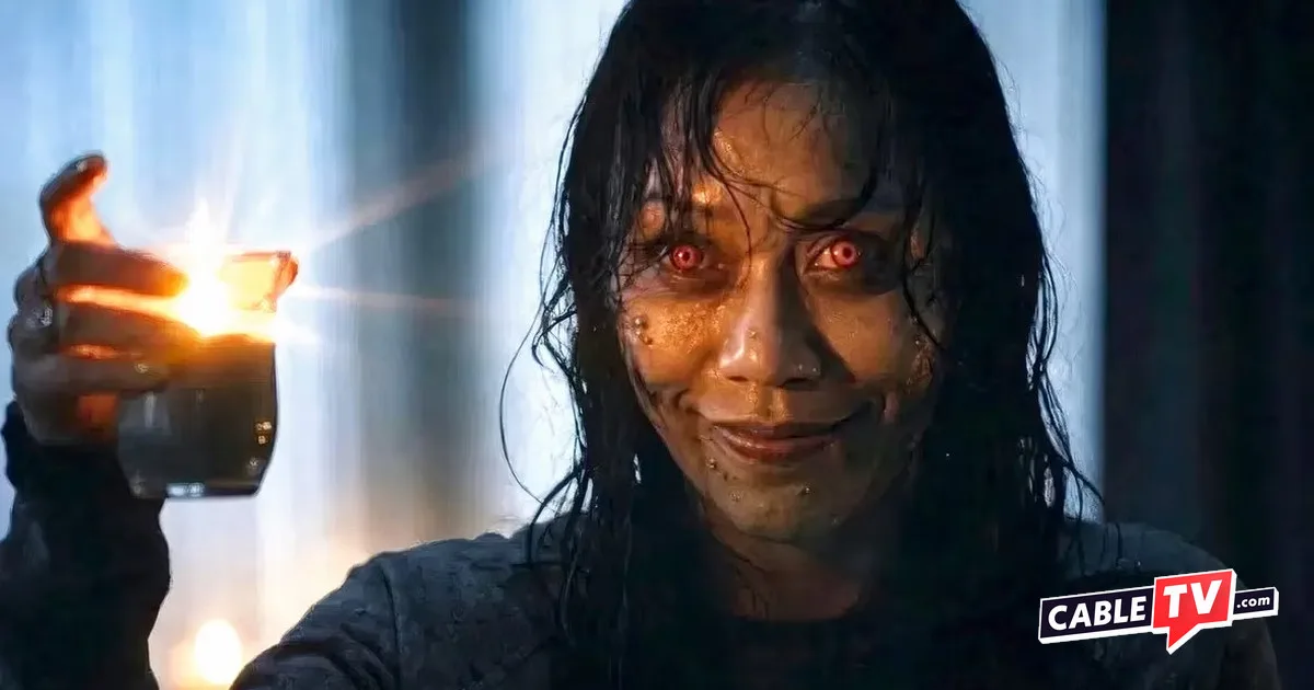 Actor Luciane Buchanan holds a candle and looks on with ghoulish red eyes and a creepy smile in 'Evil Dead Burn'