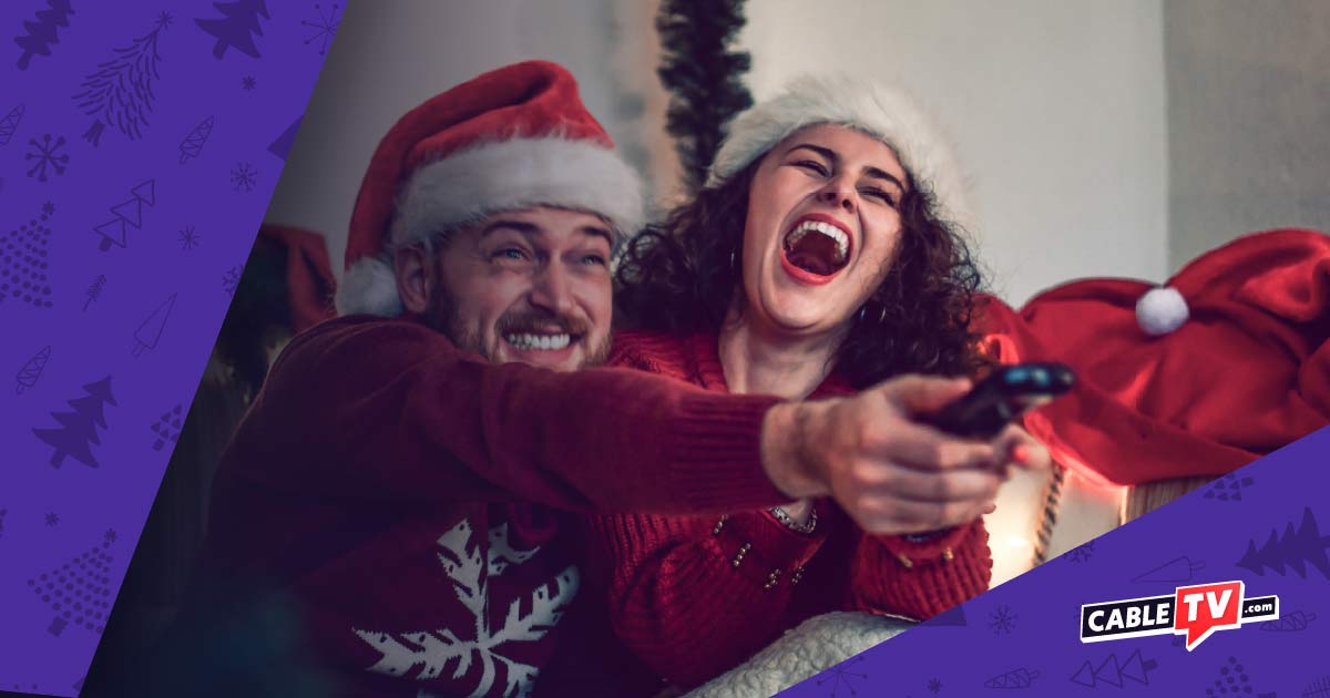 Smiling man and laughing woman in Santa hats pointing a TV remote