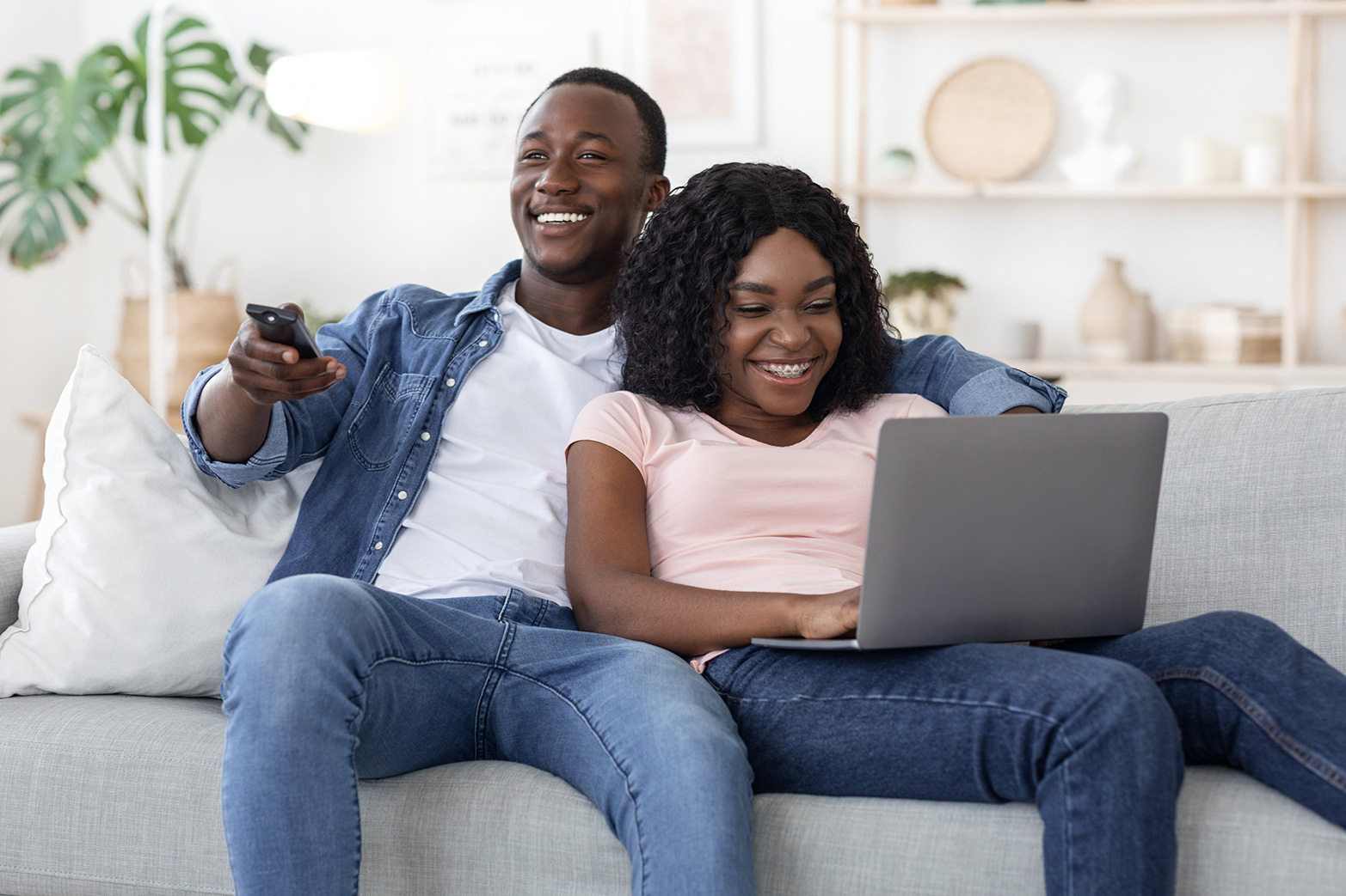 Young black couple watching TV and using a laptop at home