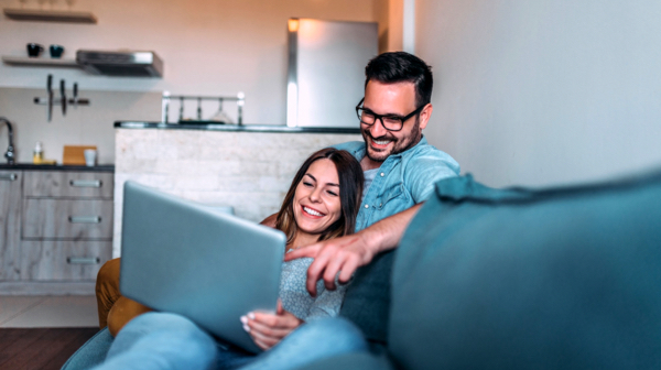 Couple laying on couch and laughing while looking at laptop