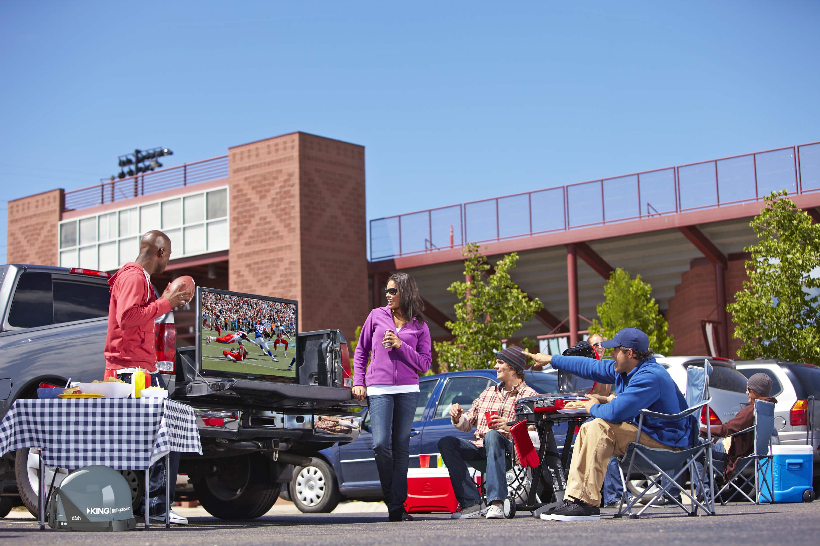 Friends tailgating outside a stadium with a TV in a truck bed