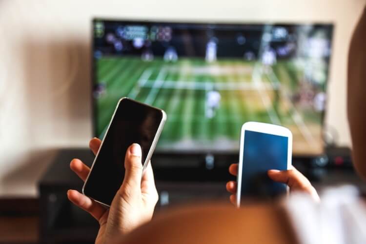 Two people holding two smartphones in front of a tv