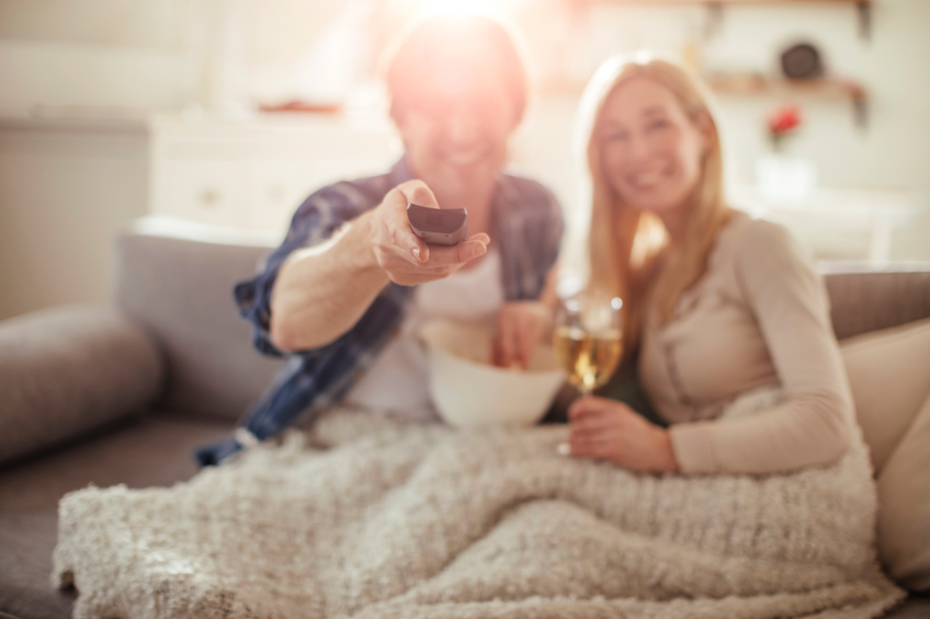 cozy couple changing tv channel with remote wrapped in a blanket with wine