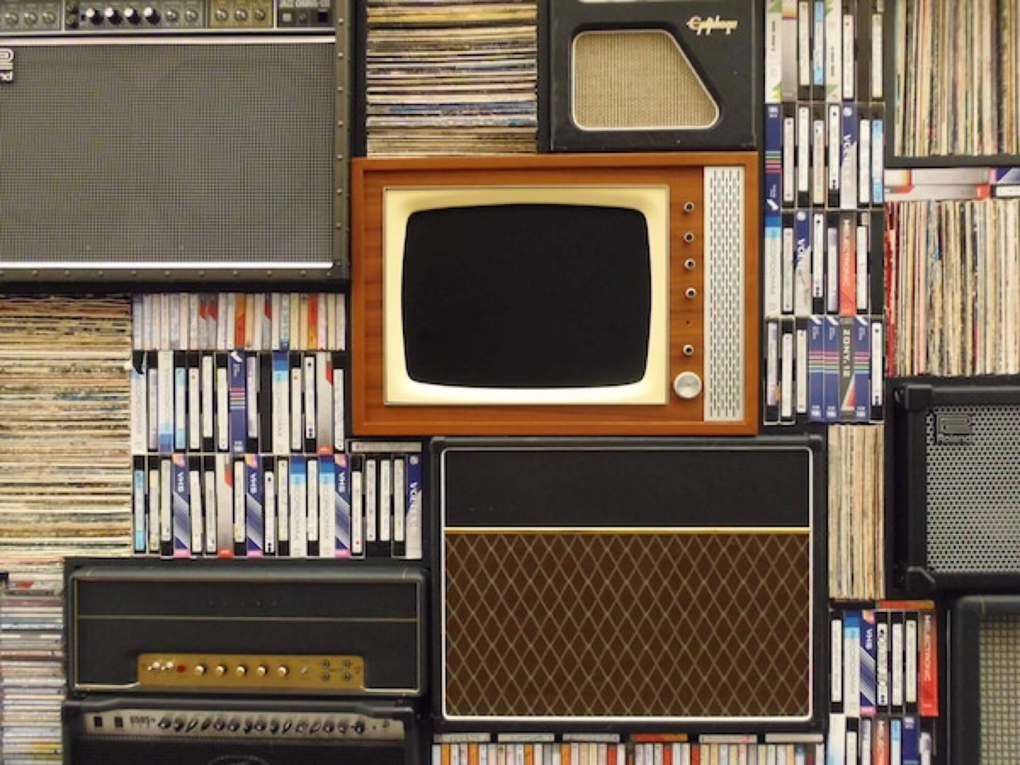 A vintage TV stacked amongst vintage speakers and tapes.